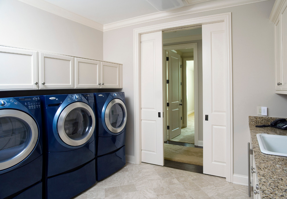 Photo of a large classic separated utility room in Chicago with a built-in sink, recessed-panel cabinets, white cabinets, beige walls, limestone flooring and a side by side washer and dryer.