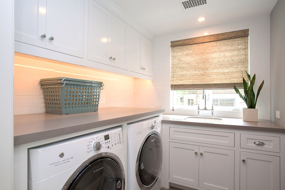Modelo de lavadero clásico renovado con fregadero bajoencimera, armarios estilo shaker, puertas de armario blancas, paredes grises, lavadora y secadora juntas y encimeras grises