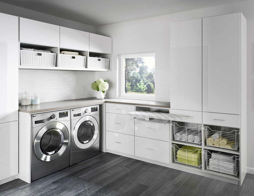 Bild på en funkis l-formad tvättstuga, med släta luckor, vita skåp, bänkskiva i kvartsit, vita väggar, klinkergolv i porslin och en tvättmaskin och torktumlare bredvid varandra