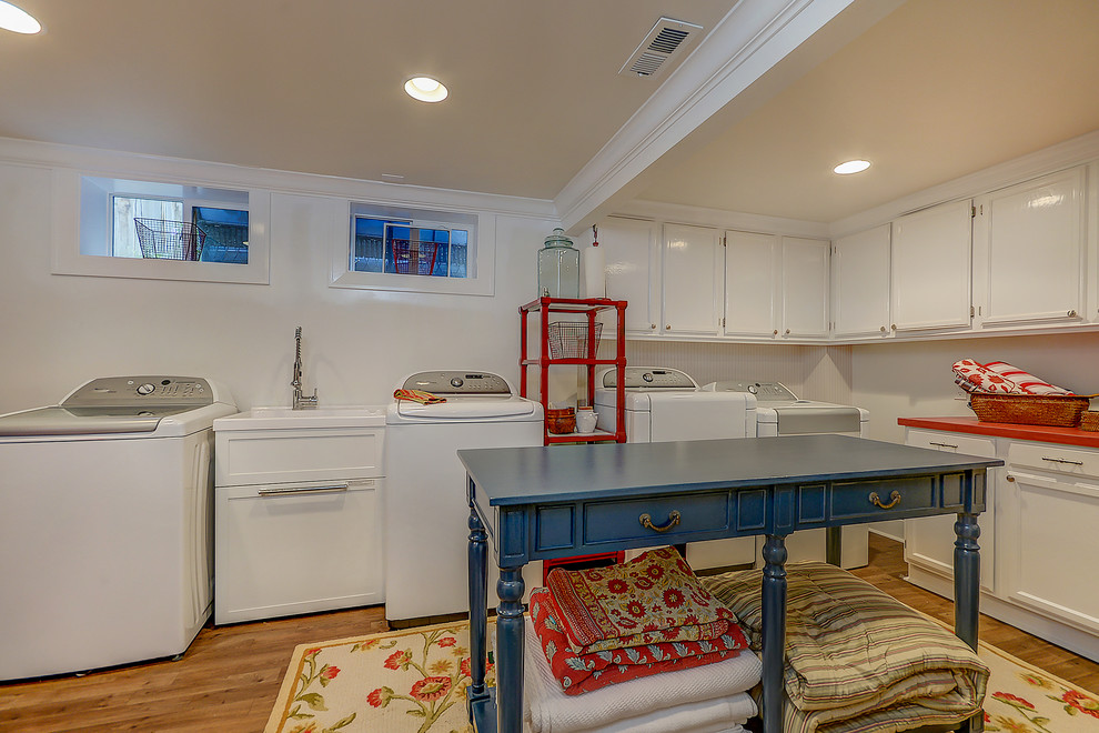 Design ideas for a large classic l-shaped utility room in Santa Barbara with an utility sink, recessed-panel cabinets, white cabinets, wood worktops, beige walls, medium hardwood flooring, a side by side washer and dryer, brown floors and red worktops.