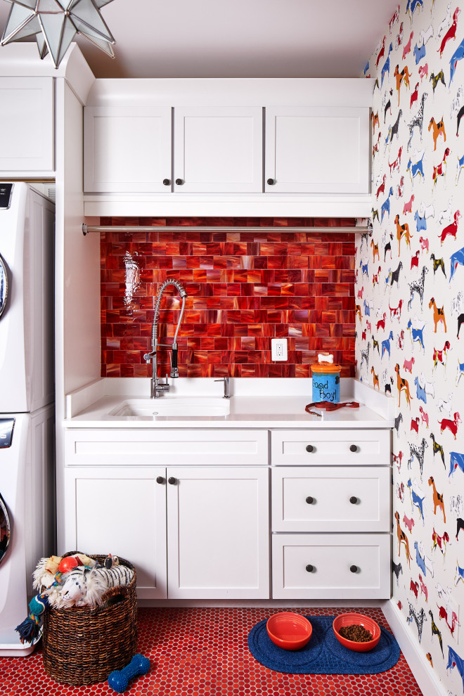 Modelo de lavadero clásico con fregadero de un seno, armarios estilo shaker, puertas de armario blancas, paredes multicolor, lavadora y secadora apiladas, suelo rojo y encimeras blancas