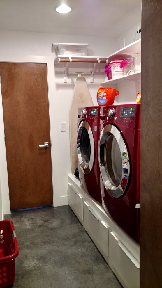 Imagen de cuarto de lavado de galera ecléctico pequeño con armarios con paneles lisos, puertas de armario blancas, paredes blancas, suelo de cemento y lavadora y secadora juntas
