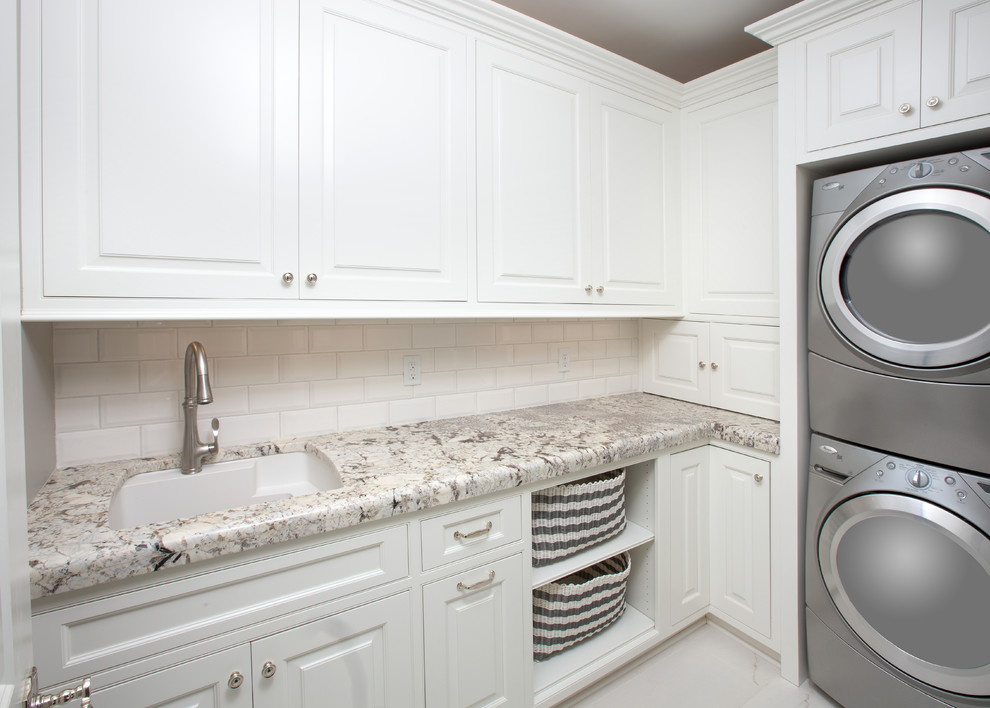 Inredning av en lantlig mellanstor u-formad tvättstuga enbart för tvätt, med en undermonterad diskho, granitbänkskiva, vita väggar, marmorgolv, en tvättpelare, luckor med profilerade fronter och vita skåp