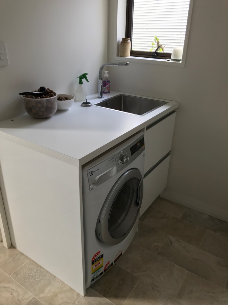 Design ideas for a small contemporary l-shaped utility room in Christchurch with a single-bowl sink, white cabinets, laminate countertops, beige walls, porcelain flooring and multi-coloured floors.