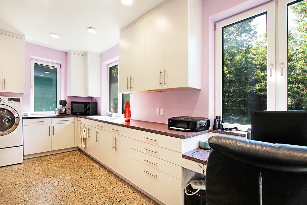 На фото: огромная п-образная универсальная комната в стиле ретро с накладной мойкой, плоскими фасадами, серыми фасадами, столешницей из ламината, розовыми стенами, бетонным полом, со стиральной и сушильной машиной рядом, разноцветным полом и разноцветной столешницей