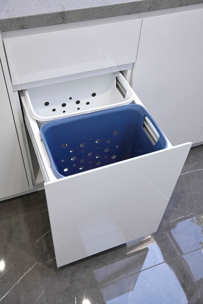 Photo of a medium sized modern galley separated utility room in Other with a built-in sink, flat-panel cabinets, white cabinets, engineered stone countertops, white walls, porcelain flooring, a concealed washer and dryer, grey floors and grey worktops.
