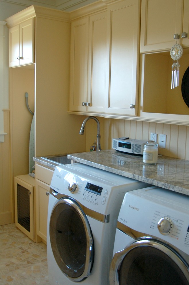 Foto på ett mellanstort maritimt grovkök, med en nedsänkt diskho, luckor med infälld panel, gula skåp, granitbänkskiva, vita väggar, en tvättmaskin och torktumlare bredvid varandra och gult golv