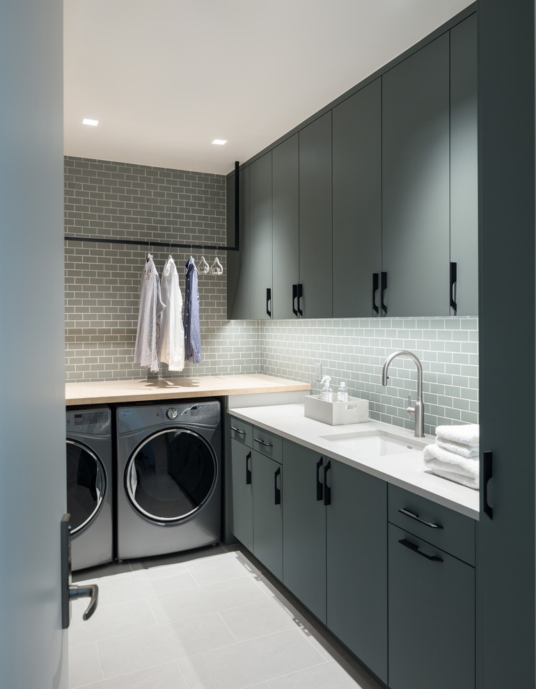 Foto di una sala lavanderia design di medie dimensioni con ante lisce, lavatrice e asciugatrice affiancate, lavello sottopiano, ante grigie, top in legno, pavimento grigio e top bianco