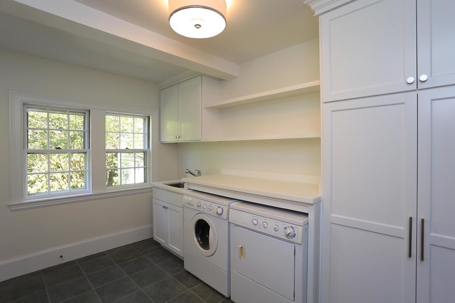 This is an example of a medium sized classic single-wall separated utility room in Portland Maine with a built-in sink, shaker cabinets, white cabinets, composite countertops, yellow walls, slate flooring and a side by side washer and dryer.