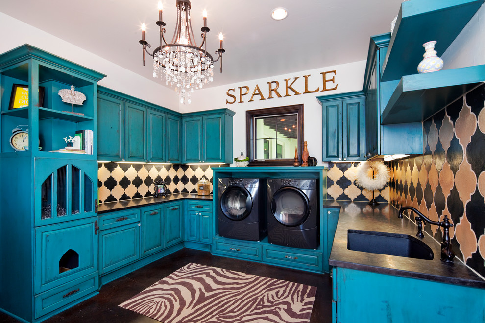 Immagine di una grande sala lavanderia chic con lavello sottopiano, ante con bugna sagomata, ante blu, pareti bianche, lavatrice e asciugatrice affiancate, pavimento marrone e top nero