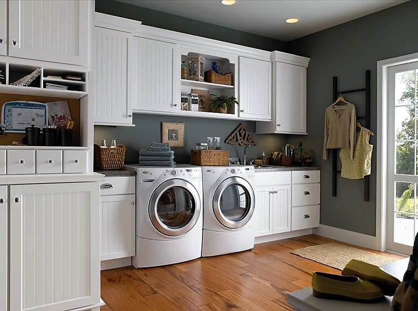 Inredning av en klassisk stor linjär tvättstuga enbart för tvätt, med en nedsänkt diskho, skåp i shakerstil, vita skåp, granitbänkskiva, grå väggar, mellanmörkt trägolv och en tvättmaskin och torktumlare bredvid varandra
