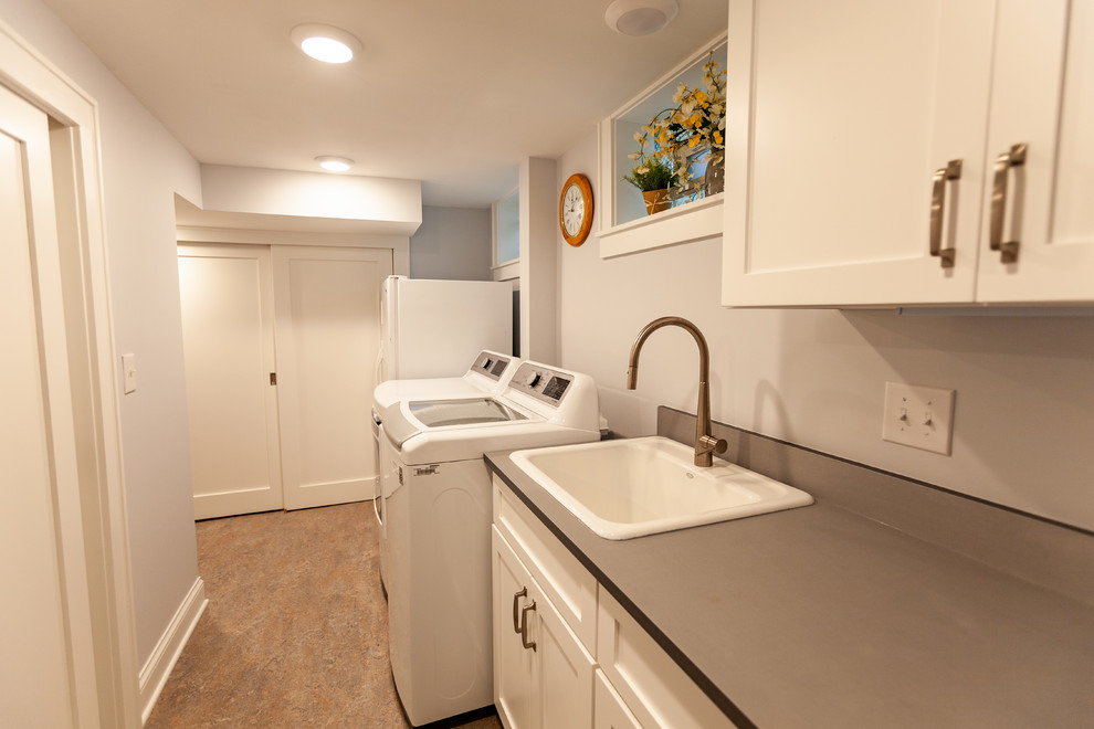 Inredning av en klassisk grå linjär grått tvättstuga enbart för tvätt, med en enkel diskho, luckor med infälld panel, vita skåp, bänkskiva i koppar, grå väggar, linoleumgolv, en tvättmaskin och torktumlare bredvid varandra och beiget golv