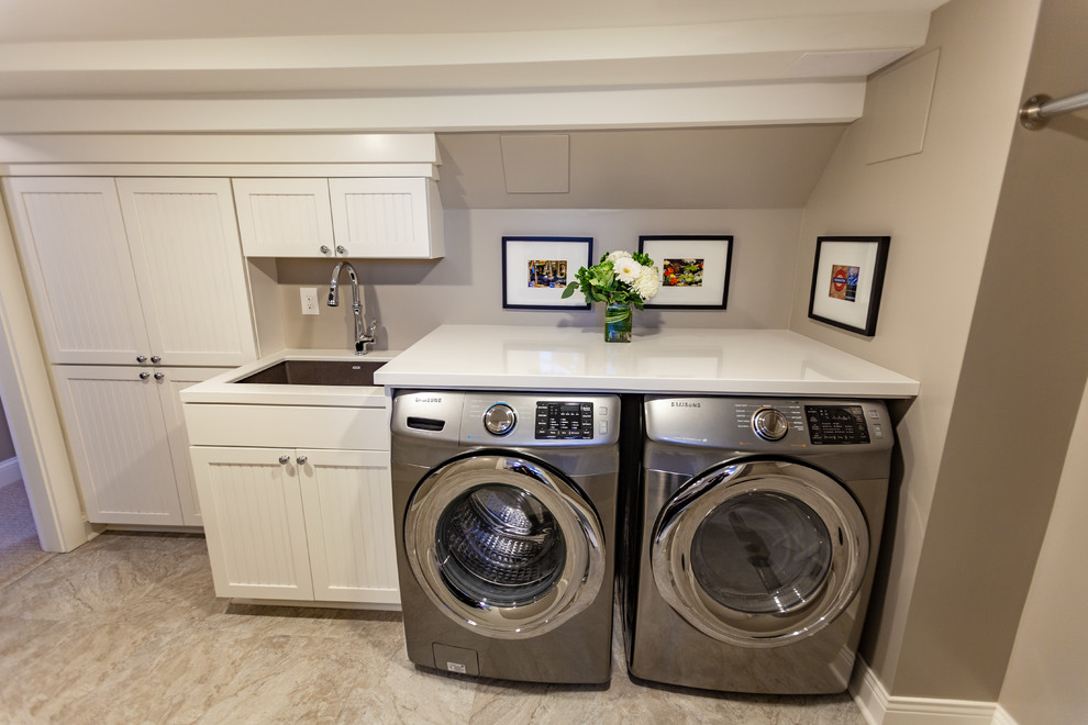 Exempel på en stor klassisk vita linjär vitt tvättstuga enbart för tvätt, med en undermonterad diskho, luckor med profilerade fronter, vita skåp, marmorbänkskiva, beige väggar, vinylgolv, en tvättmaskin och torktumlare bredvid varandra och beiget golv