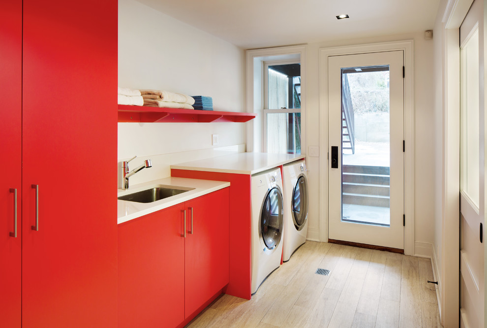 Cette photo montre une buanderie linéaire tendance avec un placard à porte plane, des portes de placard rouges, des machines côte à côte et un plan de travail blanc.