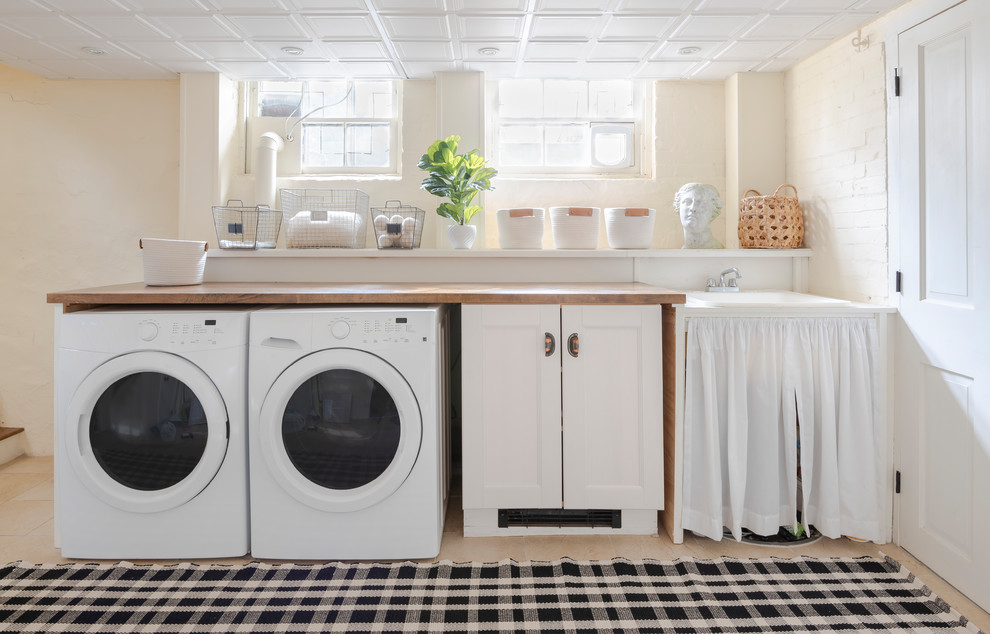 Idéer för att renovera en liten lantlig bruna linjär brunt tvättstuga enbart för tvätt, med en allbänk, skåp i shakerstil, vita skåp, träbänkskiva, vita väggar, klinkergolv i keramik, en tvättmaskin och torktumlare bredvid varandra och beiget golv