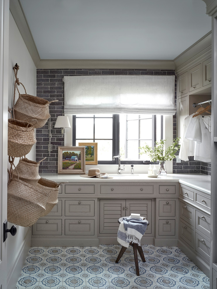 Modelo de lavadero en L de estilo de casa de campo con armarios con rebordes decorativos, puertas de armario grises, paredes grises, suelo multicolor y encimeras blancas