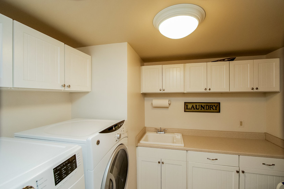 Foto på en tvättstuga, med en nedsänkt diskho, vita skåp, vita väggar och en tvättmaskin och torktumlare bredvid varandra