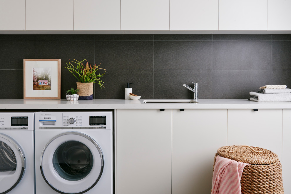 Einzeilige Moderne Waschküche mit Unterbauwaschbecken, flächenbündigen Schrankfronten, weißen Schränken, Quarzwerkstein-Arbeitsplatte und Waschmaschine und Trockner nebeneinander in Sonstige