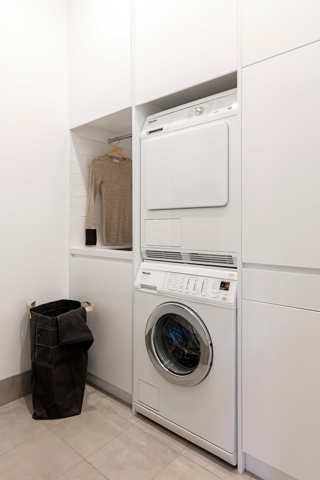 Inspiration for a mid-sized contemporary galley ceramic tile dedicated laundry room remodel in Sydney with a drop-in sink, recessed-panel cabinets, white cabinets, quartz countertops, white walls and a stacked washer/dryer