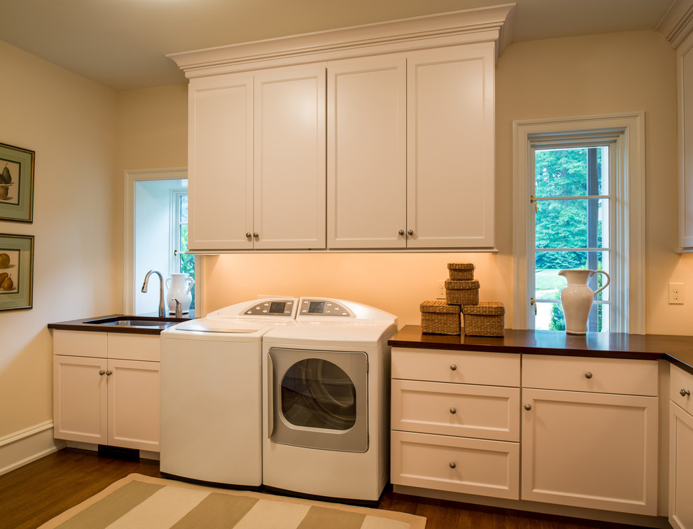 Large elegant l-shaped dedicated laundry room photo in Philadelphia with an undermount sink, recessed-panel cabinets, white cabinets, wood countertops and a side-by-side washer/dryer