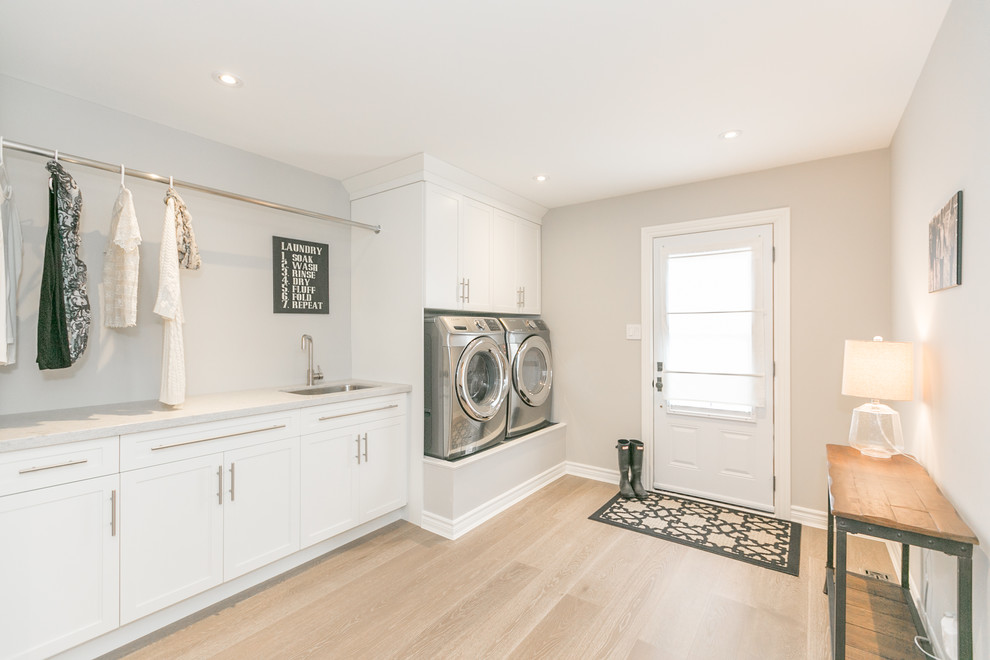 Inspiration for a large contemporary single-wall light wood floor and gray floor utility room remodel in Toronto with an undermount sink, shaker cabinets, white cabinets, quartz countertops, gray walls and a side-by-side washer/dryer