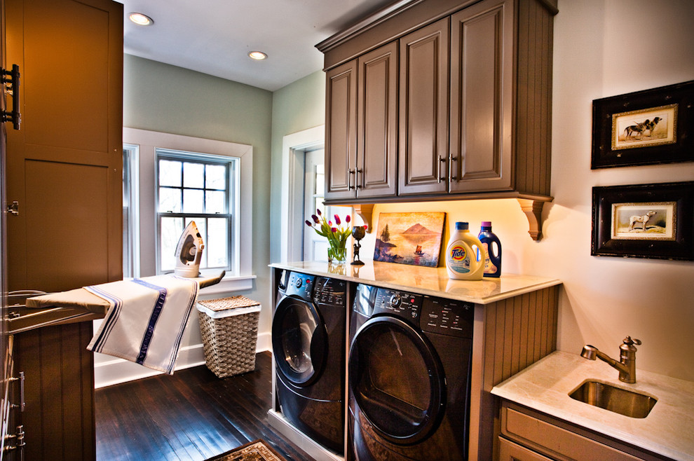 セントルイスにあるトラディショナルスタイルのおしゃれなランドリールーム (濃色木目調キャビネット、左右配置の洗濯機・乾燥機、茶色い床、ベージュのキッチンカウンター) の写真