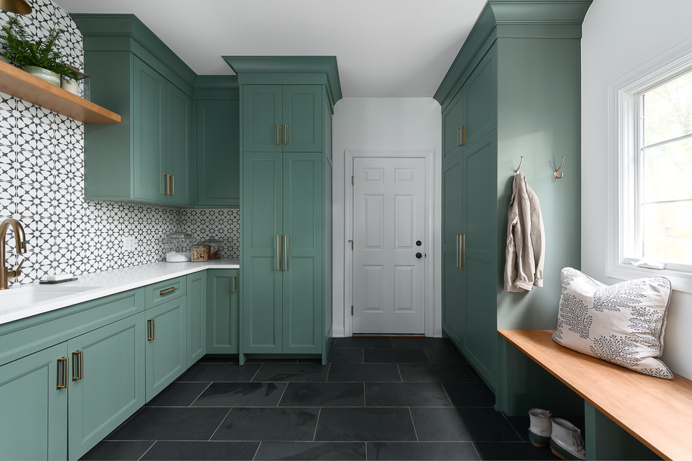 Photo of a medium sized traditional u-shaped utility room in Chicago with a submerged sink, shaker cabinets, green cabinets, engineered stone countertops, white walls, porcelain flooring, a stacked washer and dryer, black floors and white worktops.