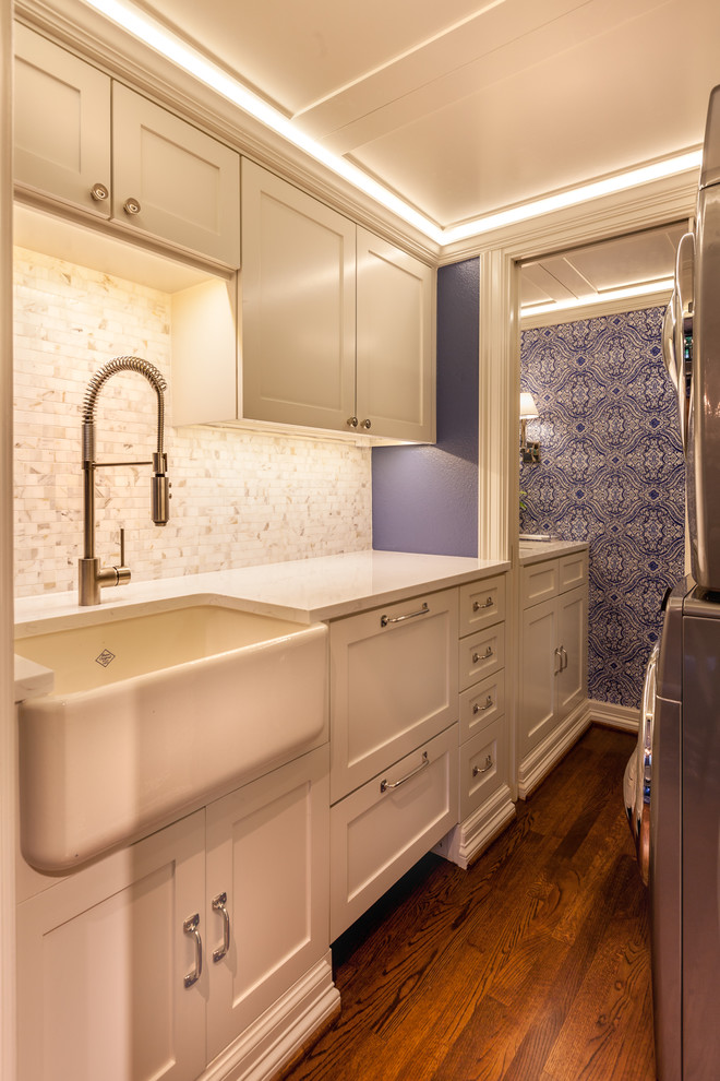Inspiration for a small classic galley separated utility room in Dallas with a belfast sink, recessed-panel cabinets, white cabinets, quartz worktops, blue walls, medium hardwood flooring and a stacked washer and dryer.