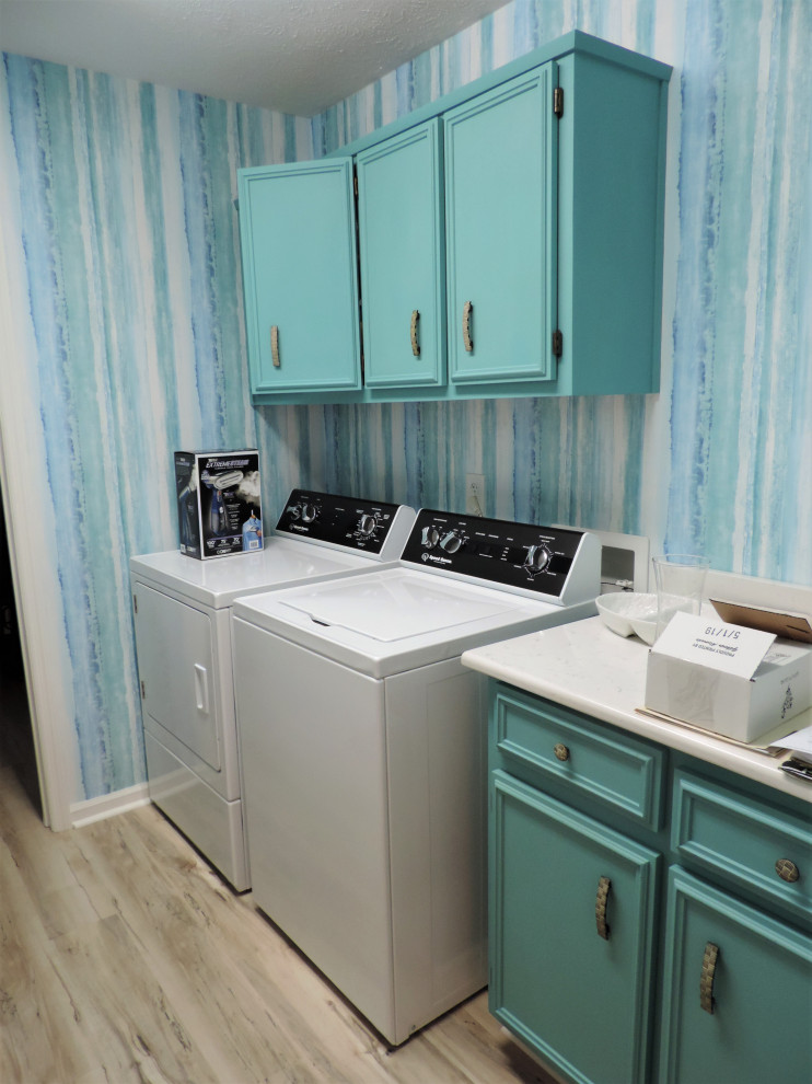 Idee per una piccola sala lavanderia stile marino con ante con bugna sagomata, ante blu, top in superficie solida, pareti multicolore, pavimento in laminato, lavatrice e asciugatrice affiancate, pavimento multicolore e top bianco