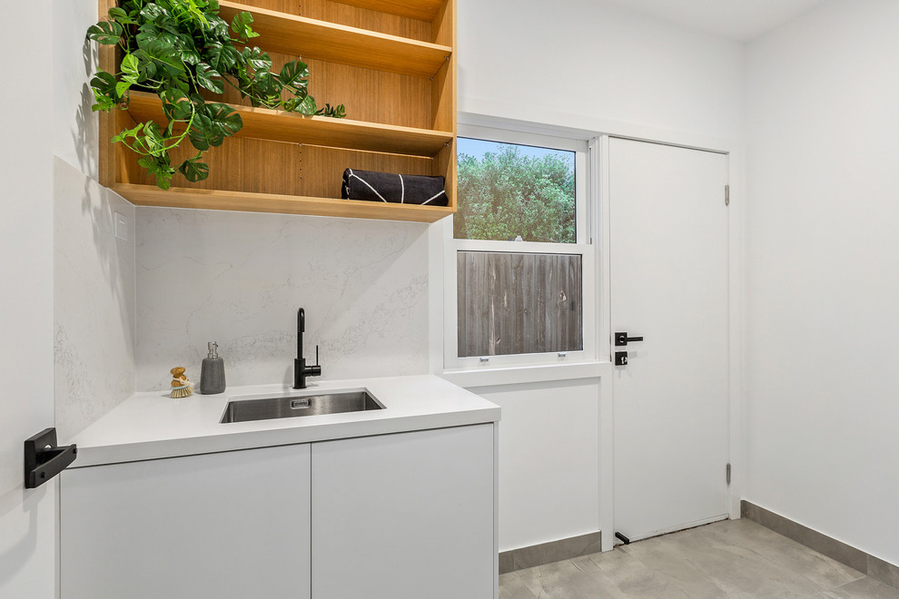 Einzeilige, Kleine Moderne Waschküche mit Unterbauwaschbecken, weißen Schränken, Quarzwerkstein-Arbeitsplatte, weißer Wandfarbe, Porzellan-Bodenfliesen, grauem Boden und weißer Arbeitsplatte in Melbourne