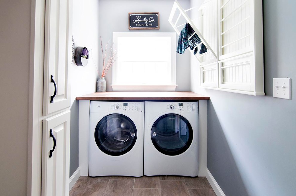 Bild på en mellanstor vintage linjär tvättstuga enbart för tvätt, med skåp i shakerstil, vita skåp, träbänkskiva, blå väggar, mellanmörkt trägolv, en tvättmaskin och torktumlare bredvid varandra och brunt golv