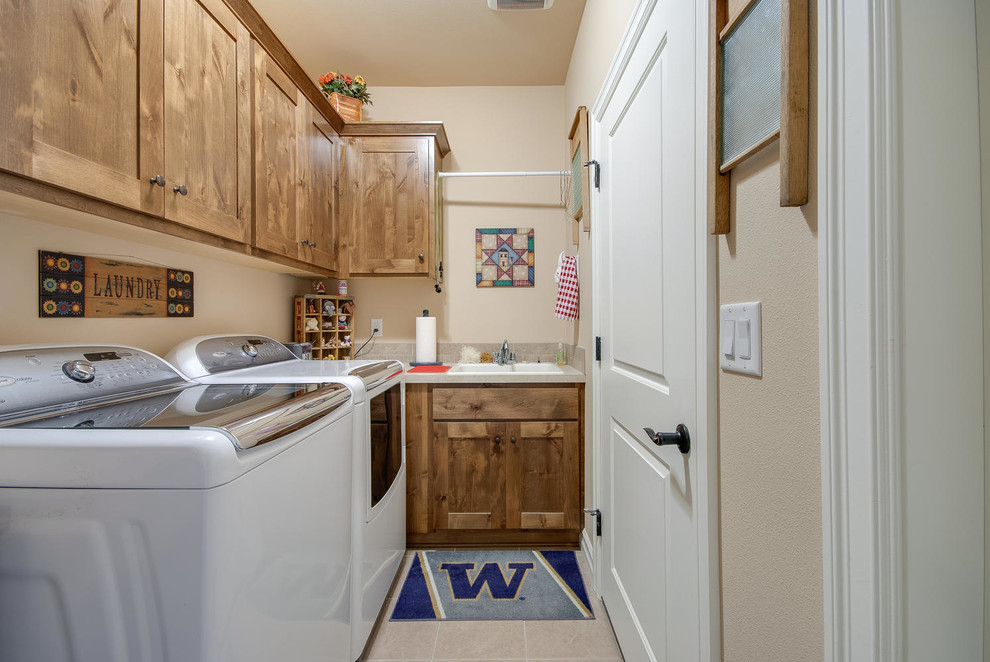 Exempel på en liten amerikansk tvättstuga enbart för tvätt, med en dubbel diskho, skåp i mellenmörkt trä, beige väggar och en tvättmaskin och torktumlare bredvid varandra