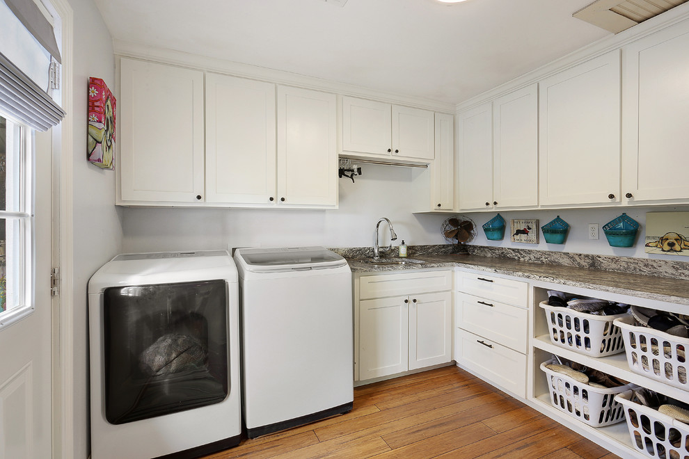 This is an example of a large classic l-shaped separated utility room in New Orleans with a submerged sink, shaker cabinets, white cabinets, granite worktops, white walls, a side by side washer and dryer, medium hardwood flooring and brown floors.
