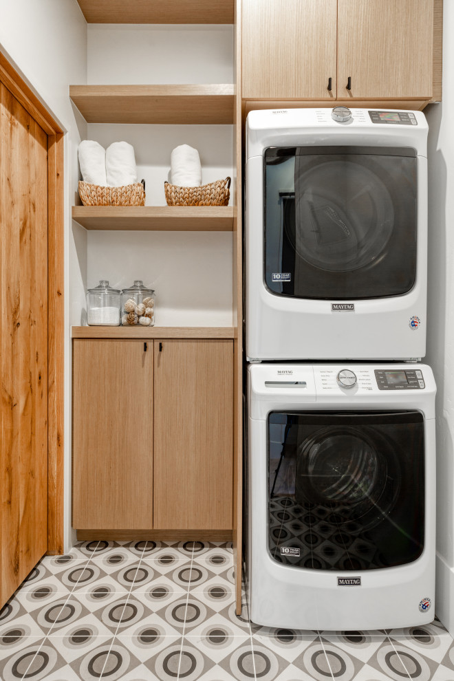 Diseño de lavadero rústico con armarios con paneles lisos, puertas de armario de madera clara, encimera de madera, paredes blancas, lavadora y secadora apiladas, suelo gris y encimeras beige