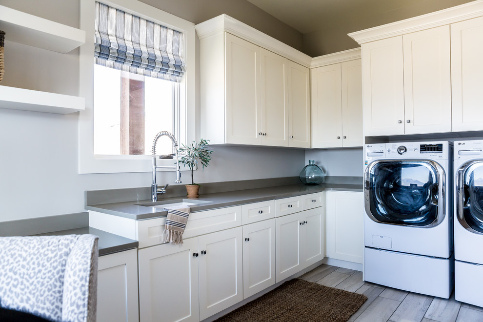 Idéer för stora lantliga l-formade grått tvättstugor enbart för tvätt, med en undermonterad diskho, luckor med infälld panel, beige skåp, grå väggar, en tvättmaskin och torktumlare bredvid varandra, bänkskiva i kvarts och klinkergolv i porslin