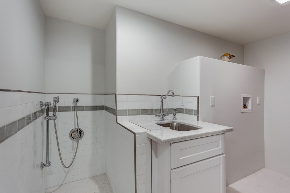 Exempel på en stor klassisk linjär tvättstuga enbart för tvätt, med en enkel diskho, luckor med infälld panel, vita skåp, marmorbänkskiva, vita väggar, klinkergolv i porslin och en tvättmaskin och torktumlare bredvid varandra
