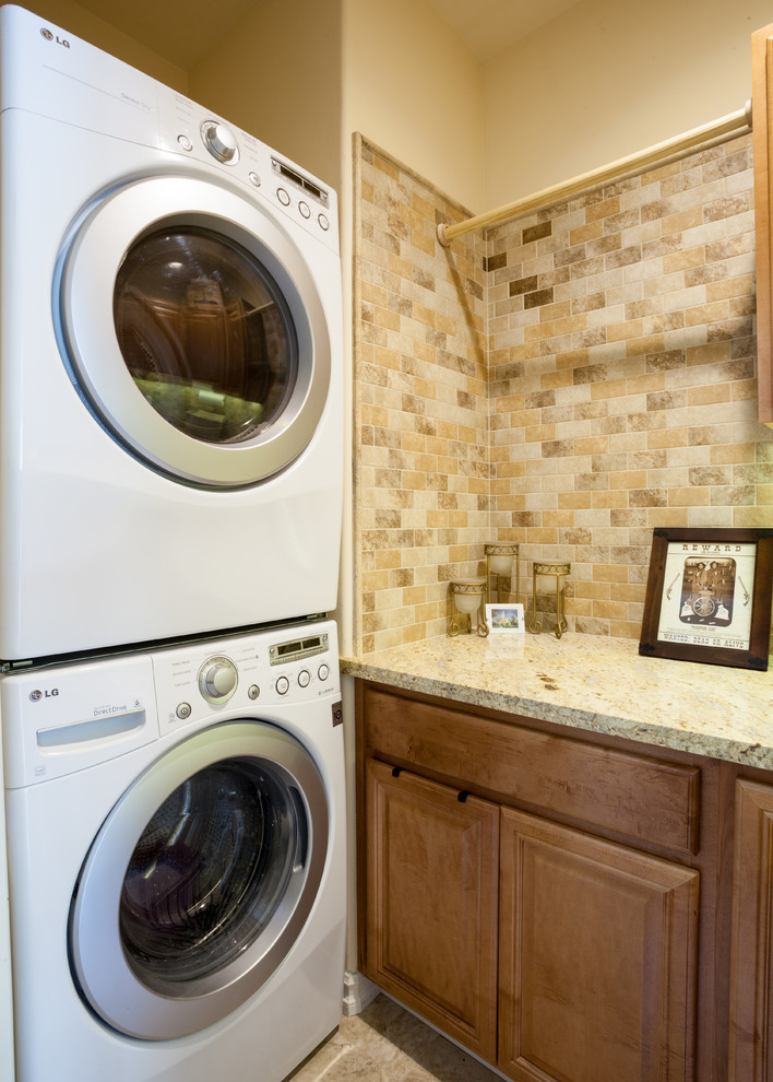 Foto på en liten vintage l-formad tvättstuga enbart för tvätt, med en undermonterad diskho, skåp i mörkt trä, granitbänkskiva, beige stänkskydd, mellanmörkt trägolv, luckor med upphöjd panel, beige väggar och en tvättpelare