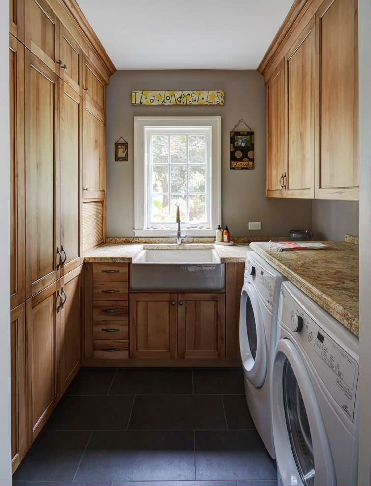 Farmhouse u-shaped separated utility room in Chicago with a belfast sink, shaker cabinets, medium wood cabinets, grey walls, a side by side washer and dryer, black floors and multicoloured worktops.