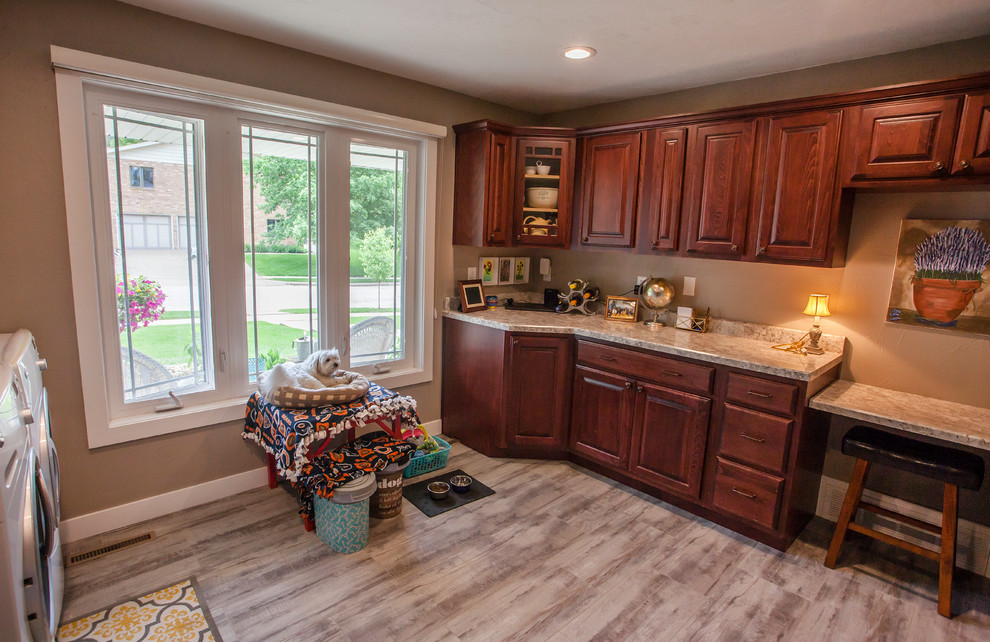This is an example of a large rural utility room in Cedar Rapids with raised-panel cabinets, red cabinets, laminate countertops, grey walls, vinyl flooring, a side by side washer and dryer, grey floors and beige worktops.