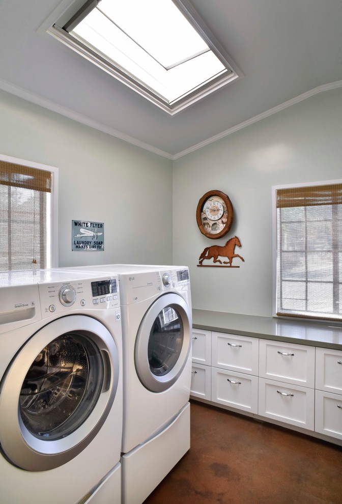 Modelo de cuarto de lavado ecléctico de tamaño medio con suelo de cemento, lavadora y secadora juntas, suelo marrón, encimeras grises, armarios estilo shaker y puertas de armario blancas
