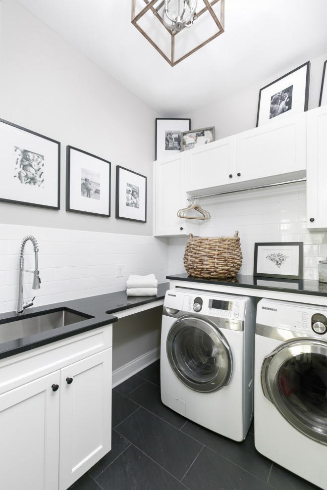 チャールストンにあるシャビーシック調のおしゃれな洗濯室 (L型、アンダーカウンターシンク、シェーカースタイル扉のキャビネット、白いキャビネット、クオーツストーンカウンター、白いキッチンパネル、セラミックタイルのキッチンパネル、ベージュの壁、セラミックタイルの床、左右配置の洗濯機・乾燥機、グレーの床、黒いキッチンカウンター) の写真