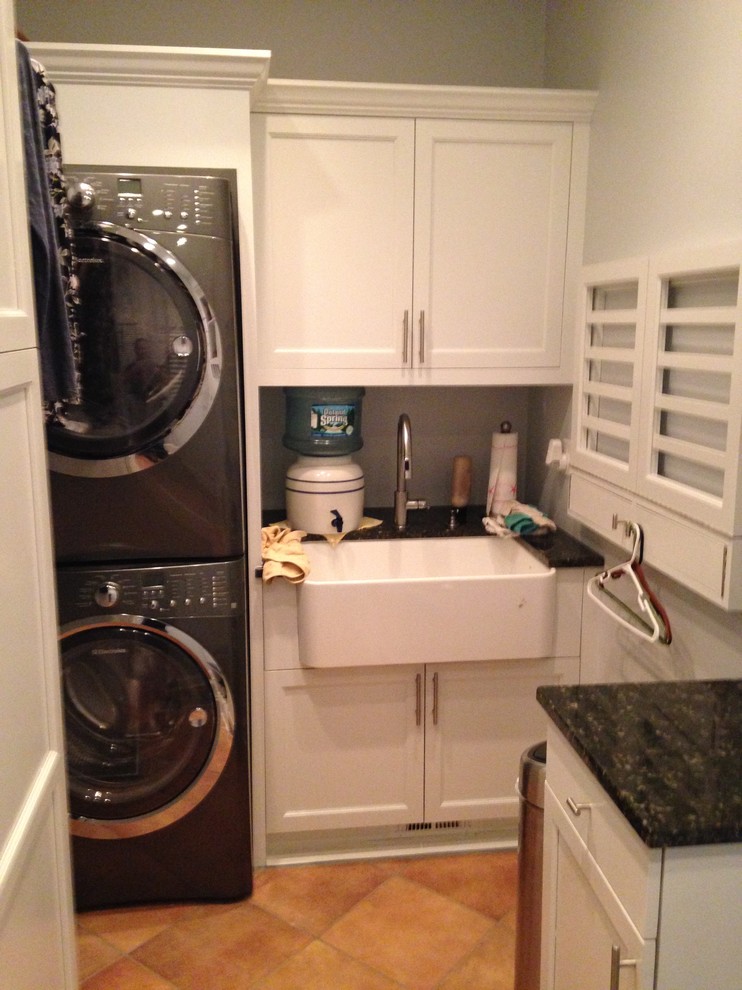 Small elegant ceramic tile dedicated laundry room photo in New York with a farmhouse sink, recessed-panel cabinets, white cabinets, granite countertops, beige walls and a stacked washer/dryer