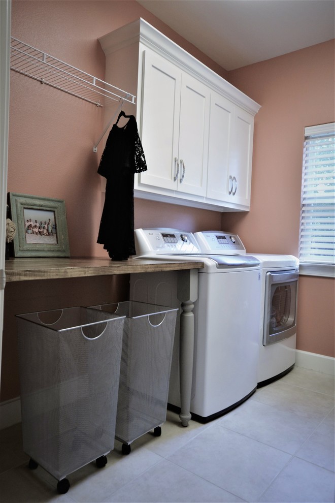 Cette photo montre une petite buanderie parallèle chic avec un placard à porte shaker, des portes de placard blanches, un plan de travail en bois, un sol en travertin, des machines côte à côte, un sol blanc et un mur rose.