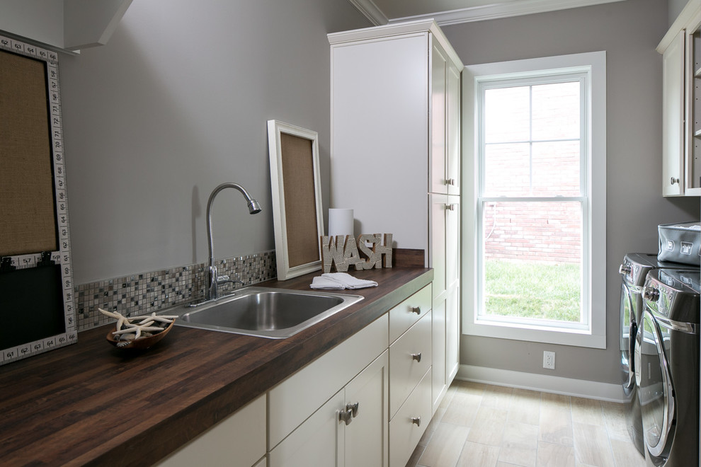 Foto på en mellanstor amerikansk tvättstuga, med en nedsänkt diskho, skåp i shakerstil, vita skåp, träbänkskiva, grå väggar, klinkergolv i porslin och beiget golv