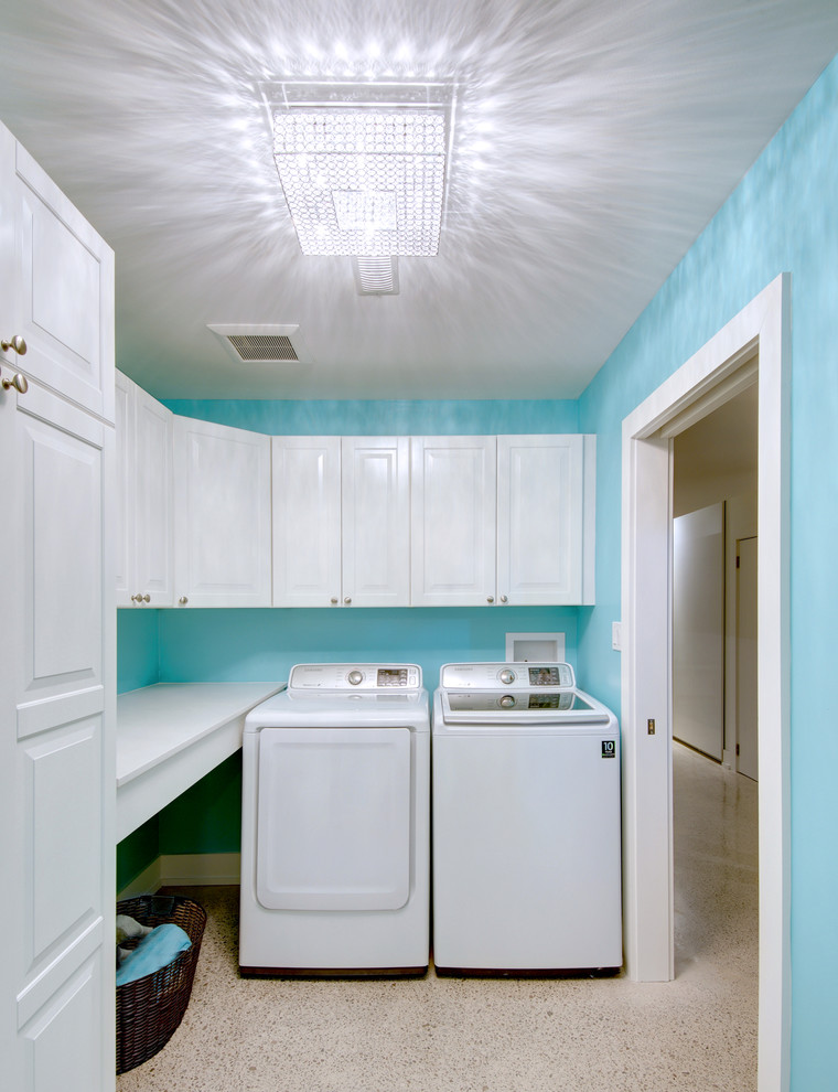 Exempel på en mellanstor modern l-formad tvättstuga enbart för tvätt, med luckor med upphöjd panel, vita skåp, bänkskiva i kvarts, blå väggar, betonggolv och en tvättmaskin och torktumlare bredvid varandra