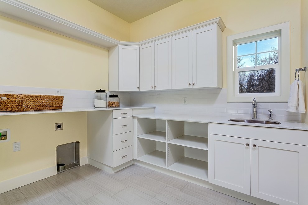 Example of a large transitional l-shaped porcelain tile utility room design in Boise with an undermount sink, recessed-panel cabinets, white cabinets, quartz countertops, yellow walls and a side-by-side washer/dryer
