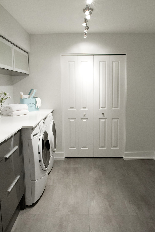 Modern inredning av en tvättstuga, med vinylgolv, en undermonterad diskho, en tvättmaskin och torktumlare bredvid varandra, bänkskiva i kvarts, grå skåp och släta luckor