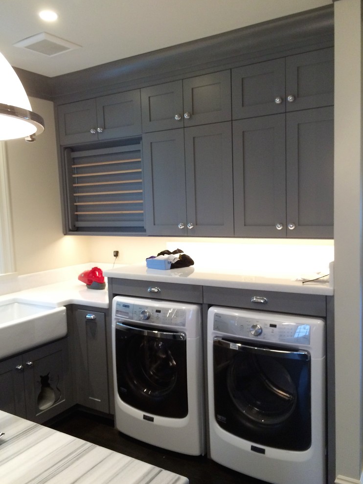 Inspiration for a large classic galley utility room in Seattle with a belfast sink, shaker cabinets, grey cabinets, beige walls, dark hardwood flooring and a side by side washer and dryer.