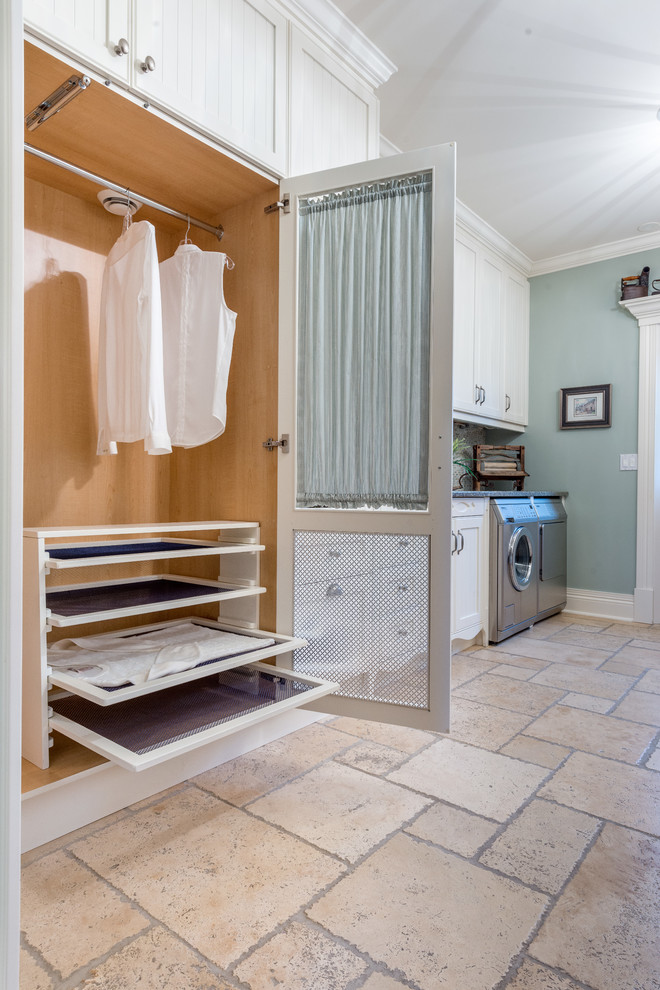 Modelo de cuarto de lavado lineal tradicional renovado de tamaño medio con armarios estilo shaker, puertas de armario blancas, paredes azules, lavadora y secadora juntas, suelo de piedra caliza y suelo beige