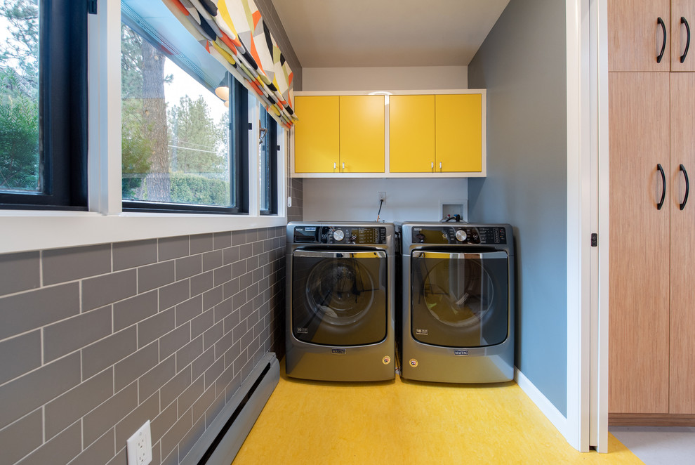 他の地域にあるミッドセンチュリースタイルのおしゃれな洗濯室 (フラットパネル扉のキャビネット、黄色いキャビネット、グレーの壁、左右配置の洗濯機・乾燥機、黄色い床) の写真